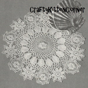 May include: A white crocheted doily with a delicate floral design. The doily is circular and has a scalloped edge. The doily is on a gray background.