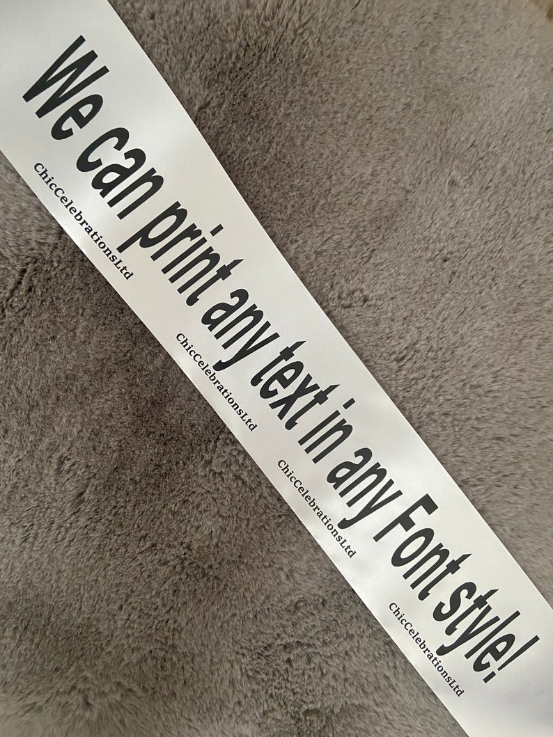 May include: White satin ribbon with the text "We can print any text in any Font style!" in black lettering. The text is repeated multiple times on the ribbon. ChicCelebrationsLtd is printed in smaller font below the text.