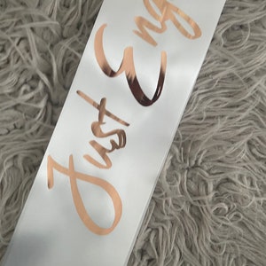May include: White satin sash with the text "Just Engaged" written in gold foil lettering.
