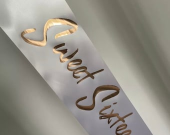 May include: White satin sash with gold foil lettering that reads "Sweet Sixteen".