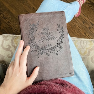 Może przedstawiać: Brązowa Biblia w skórzanej oprawie z wytłoczonym napisem "The Holy Bible" na okładce. Okładka zdobiona jest wzorem kwiatowym, a w prawym dolnym rogu wygrawerowane jest imię "Vanessa Ellerbe".