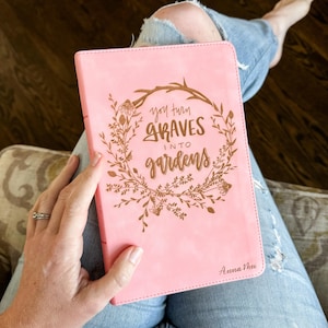 May include: Pink leather journal with a gold floral design and the text "You turn graves into gardens" and the name "Anna Mae" at the bottom.