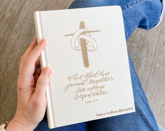 May include: A white hardcover journal with a gold cross and intertwined rings. The journal has the text "What God has joined together, let no one separate. Mark 10:9" and "Karen & Dan Benson" printed on the front cover.