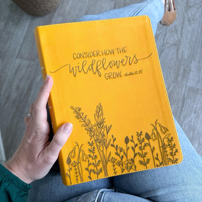 May include: A yellow journal with the text "CONSIDER HOW THE WILDFLOWERS GROW. - Luke 12:27" and a black line drawing of wildflowers on the bottom.