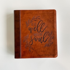 K&ouml;nnte beinhalten: Ein braunes, ledergebundenes Tagebuch mit den Worten "It is well with my soul" und einem gepr&auml;gten Blumendesign auf dem vorderen Umschlag. Der Name "Sarah Pottsgroves" ist ebenfalls auf dem Umschlag gepr&auml;gt.