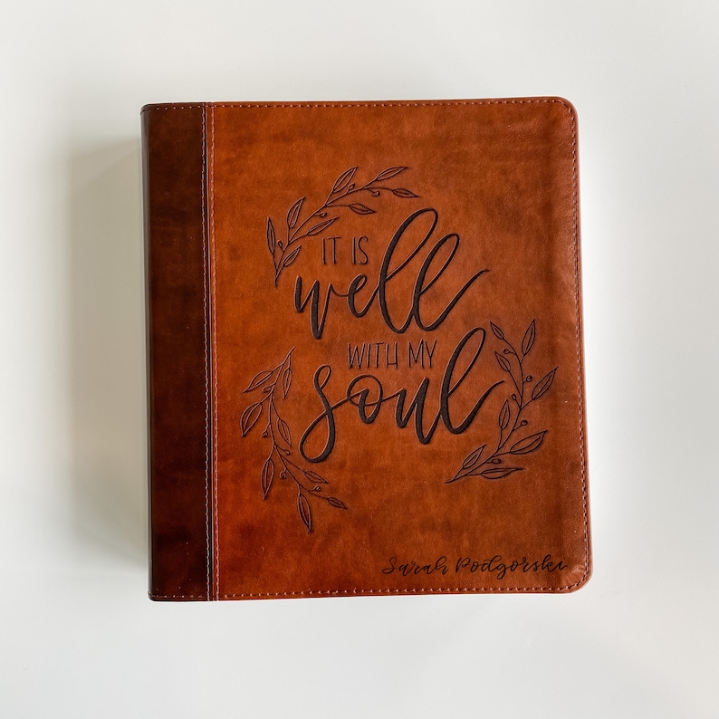 K&ouml;nnte beinhalten: Ein braunes, ledergebundenes Tagebuch mit den Worten "It is well with my soul" und einem gepr&auml;gten Blumendesign auf dem vorderen Umschlag. Der Name "Sarah Pottsgroves" ist ebenfalls auf dem Umschlag gepr&auml;gt.