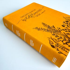 May include: A yellow leather-bound Christian Standard Bible with the text "Consider how the wildflowers grow - Luke 12:27" on the cover. The cover also features a gold embossed design of wildflowers.