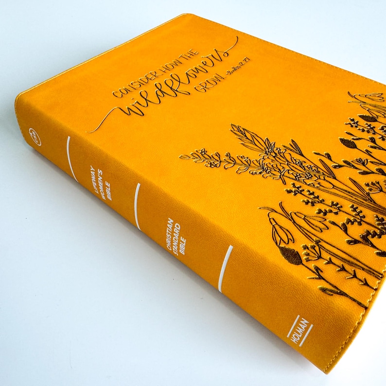 May include: A yellow leather-bound Christian Standard Bible with the text "Consider how the wildflowers grow - Luke 12:27" on the cover. The cover also features a gold embossed design of wildflowers.