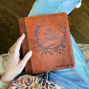 May include: A brown leather-bound Bible with a floral design and the words "The Holy Bible" embossed on the front cover. The name "Karen Joy" is also embossed on the bottom of the cover.