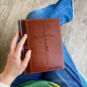 May include: A brown leather-bound journal with a cross and the word "faith" engraved on the front cover. The name "Sarah Catherine" is also engraved on the bottom of the cover.