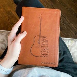 Puede incluir: Un diario de cuero marrón con un diseño de guitarra y el texto "Estad pues firmes en la libertad con que Cristo nos hizo libres Galatas 5:1" y el nombre "Caleb Daniel Benson".