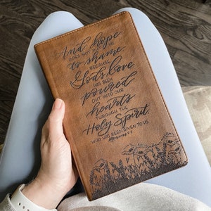 May include: A brown leather-bound journal with a floral design and the quote "And hope does not put us to shame, because God's love has been poured out into our hearts through the Holy Spirit, who has been given to us."  Romans 5:5