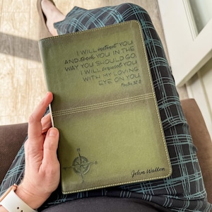 May include: Olive green leather-bound book with stitched edges. The cover features the text "I WILL instruct YOU...EYE ON YOU. Psalm 32:8" and a compass rose design. The name "John Walton" is also printed on the cover.