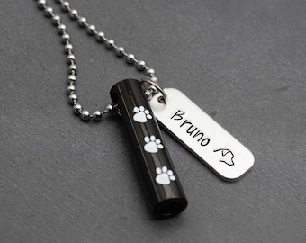 Puede incluir: Un collar de cadena plateada con un colgante cilíndrico negro con huellas de patas blancas y una etiqueta plateada grabada con "Bruno" y una huella de pata.
