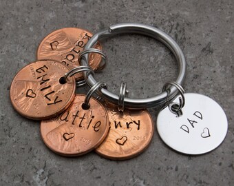 May include: A silver key chain with five copper penny charms. The charms are engraved with the names "Emily", "Katie", "Henry", "Dad" and a heart. Each penny charm has a year engraved on it.