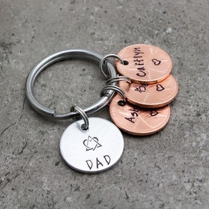 May include: Silver keychain with a silver charm that says "DAD" with a heart and arrow design. The keychain also has four copper penny charms with the names "Ashlyn", "Katelyn", "Caitlyn", and a heart on each.