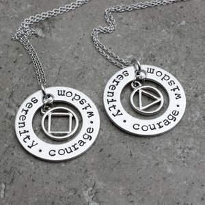 May include: Two silver necklaces with circular pendants. Each pendant features a different symbol, a triangle and a square, with the words "Serenity, Courage, I'm Hopeful" and "Serenity, Courage, I'm Hopeful" engraved around the edge.