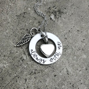 May include: Silver necklace with a round pendant that says "always with me". The pendant has a small heart-shaped urn in the center and a small angel wing charm attached to the side.
