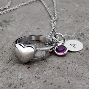 Op de afbeelding: Een zilveren ketting met een ringbedel, een hartbedel, een kleine paarse edelsteenbedel en een zilveren bedel met de letter 'A' erop.