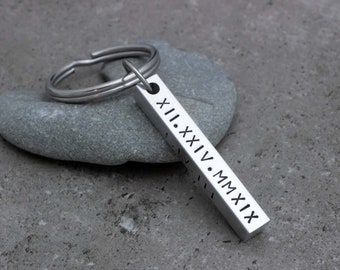 May include: A silver rectangular keychain with Roman numerals engraved on one side. The keychain is attached to a silver split ring. The text on the keychain reads XII.XXIV.MMXIX.