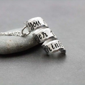 K&ouml;nnte beinhalten: Eine silberne Halskette mit drei &uuml;bereinanderliegenden Ringen. Die Ringe sind mit den Worten "you are", "bigger" und "than you think" graviert.