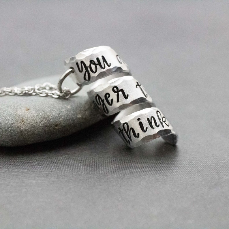 K&ouml;nnte beinhalten: Eine silberne Halskette mit drei &uuml;bereinanderliegenden Ringen. Die Ringe sind mit den Worten "you are", "bigger" und "than you think" graviert.