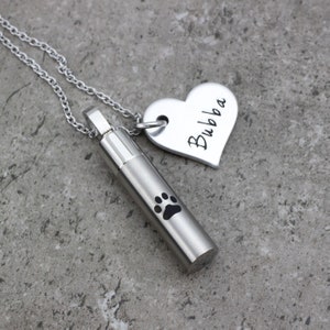 May include: Silver necklace with a heart charm engraved with the name "Bubba" and a cylindrical cremation urn pendant with a paw print.