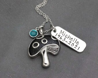 May include: Silver necklace with a mushroom charm and a tag that reads "Michelle 1963-2021". The mushroom charm has a black enamel finish and a teal crystal.