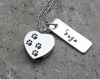 May include: Silver heart-shaped cremation necklace with paw prints and a silver tag engraved with the name "Suga".
