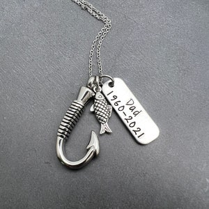 May include: Silver necklace with a fishing hook charm, a small fish charm, and a rectangular tag with the text "Dad 1960-2021".