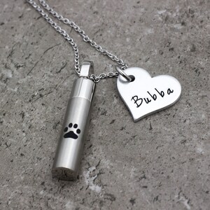 May include: Silver necklace with a heart charm engraved with the name "Bubba" and a cylindrical charm with a paw print.