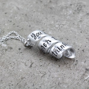 K&ouml;nnte beinhalten: Silberne Halskette mit drei verbundenen Ringen. Jeder Ring tr&auml;gt eine eingravierte Aufschrift: "you", "are", "stronger than you think".