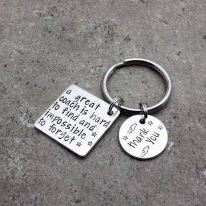 May include: Silver keychain with two tags. The larger tag is square and says "A great coach is hard to find and impossible to forget." The smaller tag is round and says "Thank You" with a wing design.