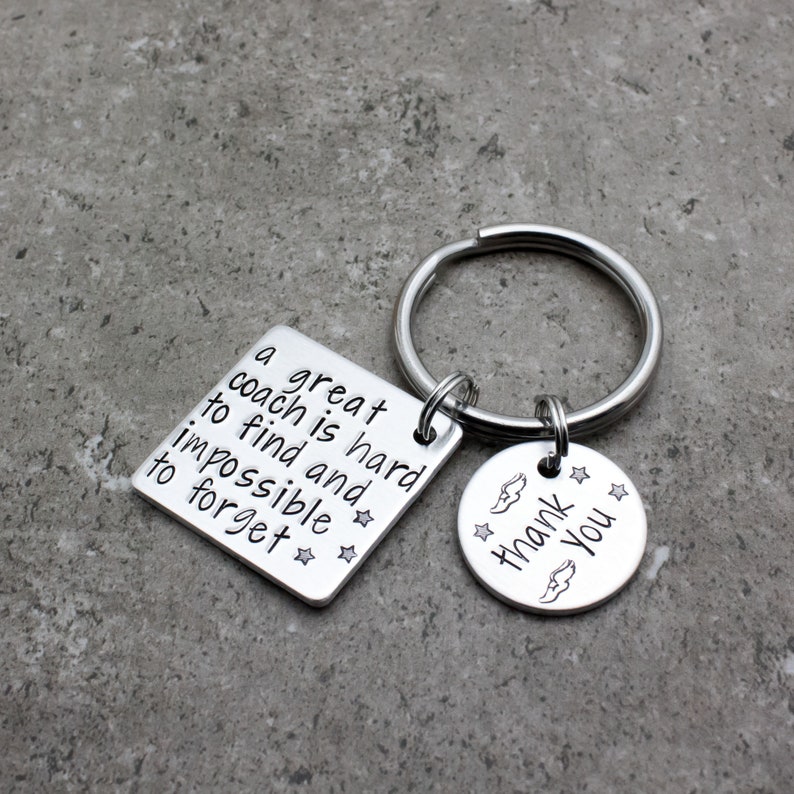 May include: Silver keychain with two tags. The larger tag is square and says "A great coach is hard to find and impossible to forget." The smaller tag is round and says "Thank You" with a wing design.
