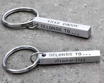 May include: Two silver keychains with a bar-shaped charm. The top charm reads "This Daddy Belongs To..." and the bottom charm reads "Belongs To... Winnie May".
