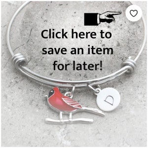 May include: Silver bangle bracelet with a red cardinal charm and a silver charm with the letter D. The bracelet has a click here to save an item for later text.