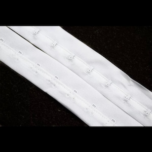 Hook and eye tape tape fastener . One line hook and eye tape in white .hook and eye for grabs and corset fastening .