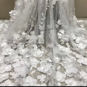 May include: White floral lace fabric with 3D flowers and pearl embellishments. The fabric is sheer and delicate, perfect for special occasion garments.