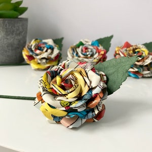 May include: Four colorful paper roses made from comic book pages. The roses are arranged in a row with a green leaf stem.