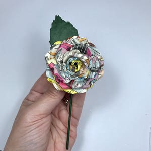 May include: A single, handmade rose made from colorful comic book pages. The rose is attached to a green stem.