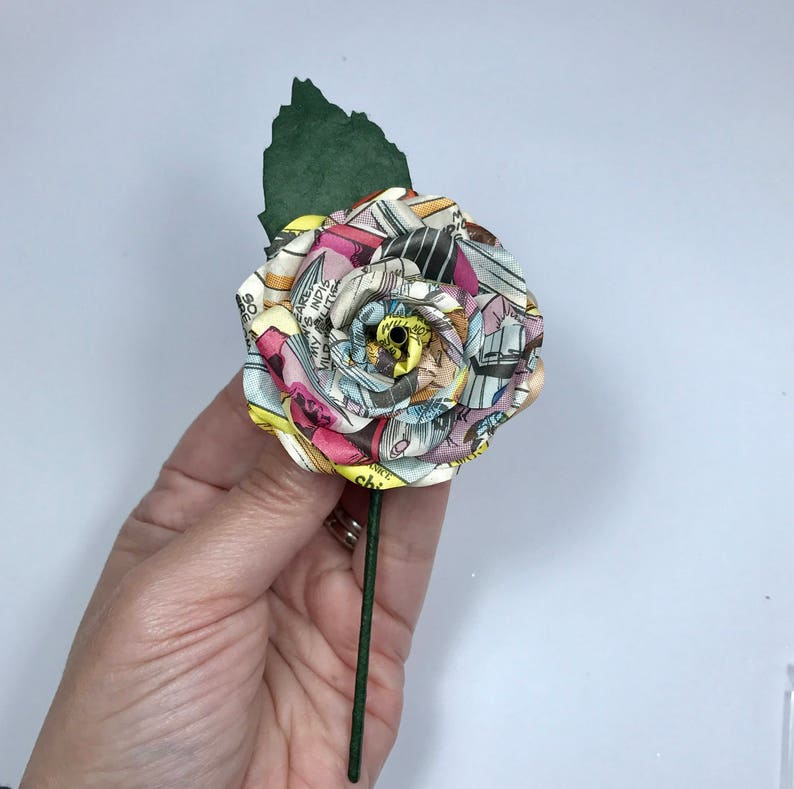 May include: A single, handmade rose made from colorful comic book pages. The rose is attached to a green stem.