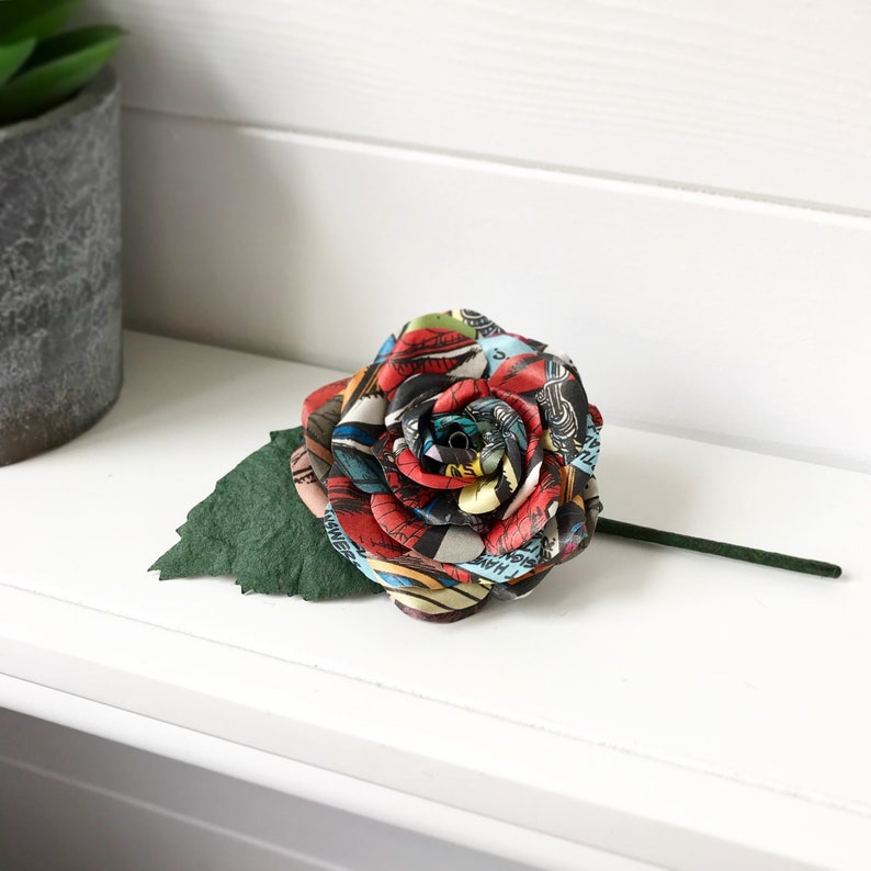 May include: A single red, blue, and yellow comic book rose with a green leaf stem.