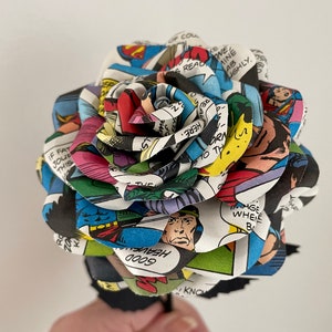 Puede incluir: Una rosa de tallo negro hecha de p&aacute;ginas de c&oacute;mics con Superman. La rosa est&aacute; hecha de m&uacute;ltiples capas de p&aacute;ginas de c&oacute;mics, con el texto "HEAVEN GOOD" visible en una de las capas.