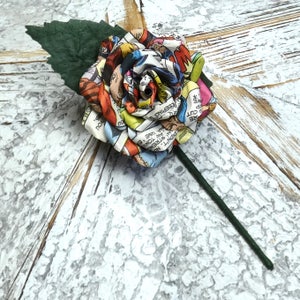 May include: A colorful comic book rose with a green stem and leaf. The rose is made of fabric and has a vintage comic book pattern. The text on the comic book fabric reads "KEEPING YOU", "CUT", "DIDN'T", "AN STRENG", "AN TONIG", "NA USE 'E", "REEPING", "YOU", "S."