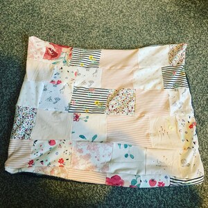 May include: A patchwork quilt with a pink and white striped background. The quilt is made of various fabrics with floral patterns and a few with animal prints. The quilt has the words "love nature" embroidered on it.