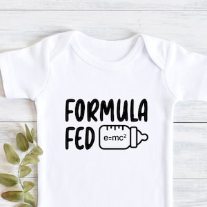 Peut inclure: Combinaison bébé blanche avec un texte noir qui dit "Formula Fed e=mc2" et une illustration noir et blanc d'un biberon.