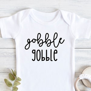 Könnte beinhalten: Weißer Baby-Strampler mit schwarzem Text, der "gobble gobble" lautet.