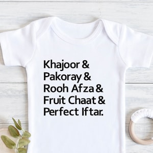 May include: White baby grow with black text that reads "Khajoor & Pakoray & Rooh Afza & Fruit Chaat & Perfect Iftar."