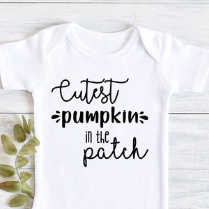 Könnte beinhalten: Weißer Baby-Strampler mit schwarzem Text, der "Cutest pumpkin in the patch" lautet.