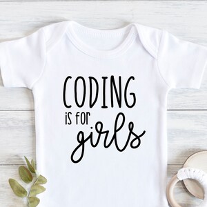 Peut inclure: Combinaison blanche pour bébé avec un texte noir qui dit "Coding is for girls".